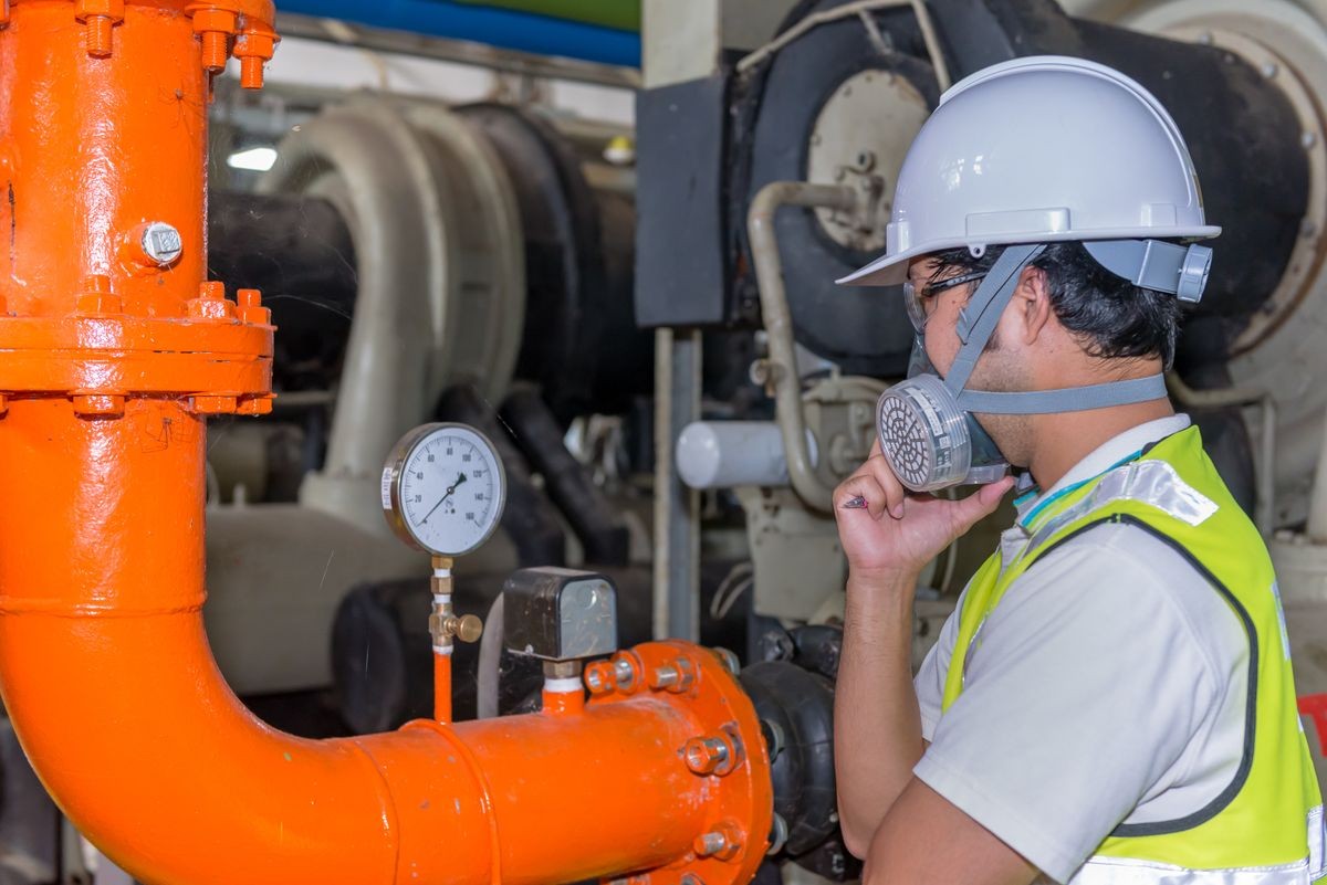 Asian engineer wearing glasses working in the boiler room,maintenance checking technical data of heating system equipment,Thailand people Wearing a gas mask